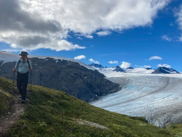 Ein Wanderer auf einem grasbewachsenen Grat neben einem großen Gletscher.