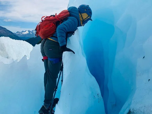 Ein Kletterer mit Helm und Rucksack, der auf einem Gletscher in eine tiefe Gletscherspalte blickt.