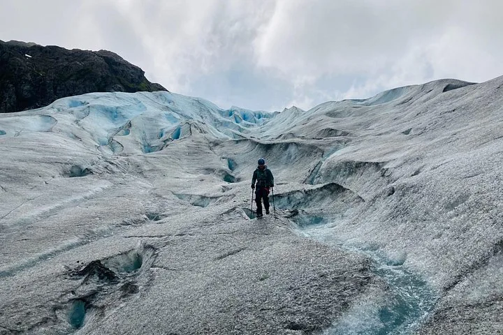 Ein Wanderer mit Stöcken auf einem großen, strukturierten Gletscher.