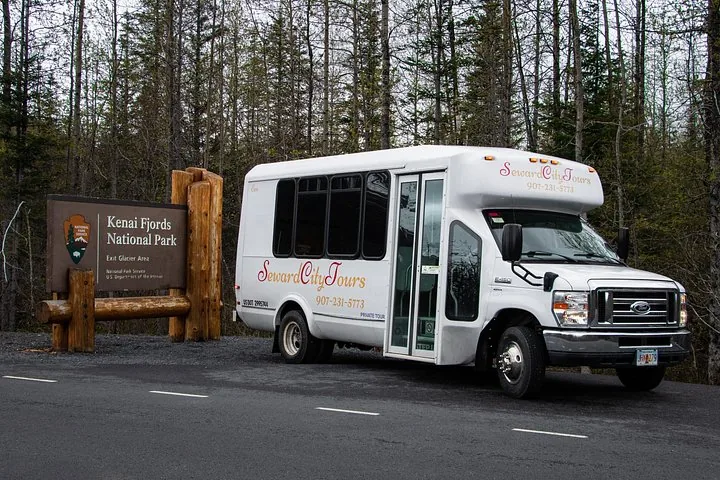 Ein Shuttlebus von Seward City Tours, der neben dem Schild des Kenai-Fjords-Nationalparks parkt.