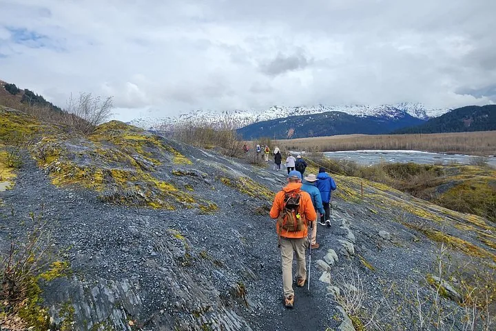 Wanderer auf einem steinigen Weg mit schneebedeckten Bergen in der Ferne.