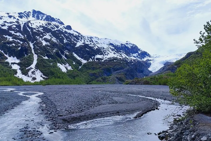 Ein steiniges Flussbett, das auf einen Gletscher und schneebedeckte Berge zuführt.